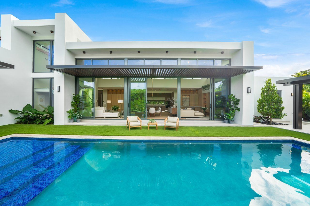 A modern white home with floor-to-ceiling glass beside a long pool in Biscayne Park