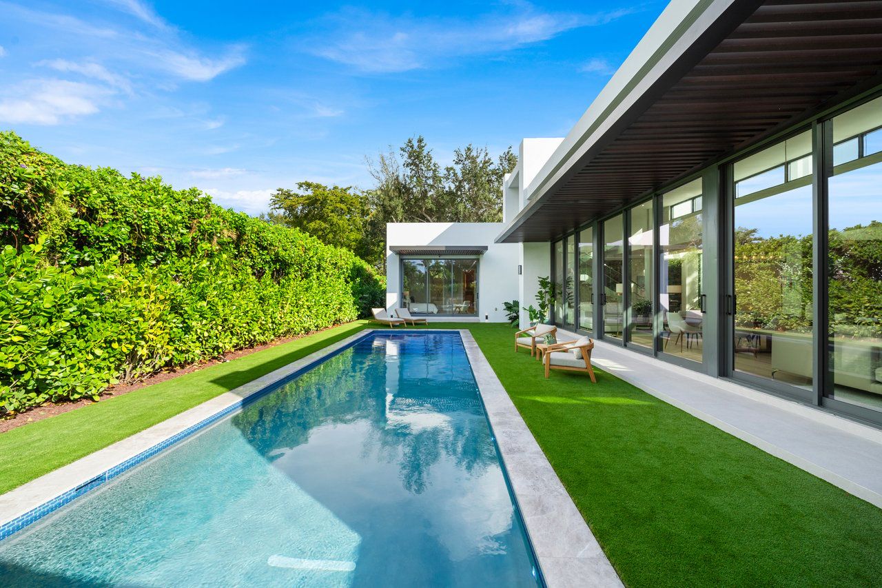 Long lap pool between a glass wall and a green hedge