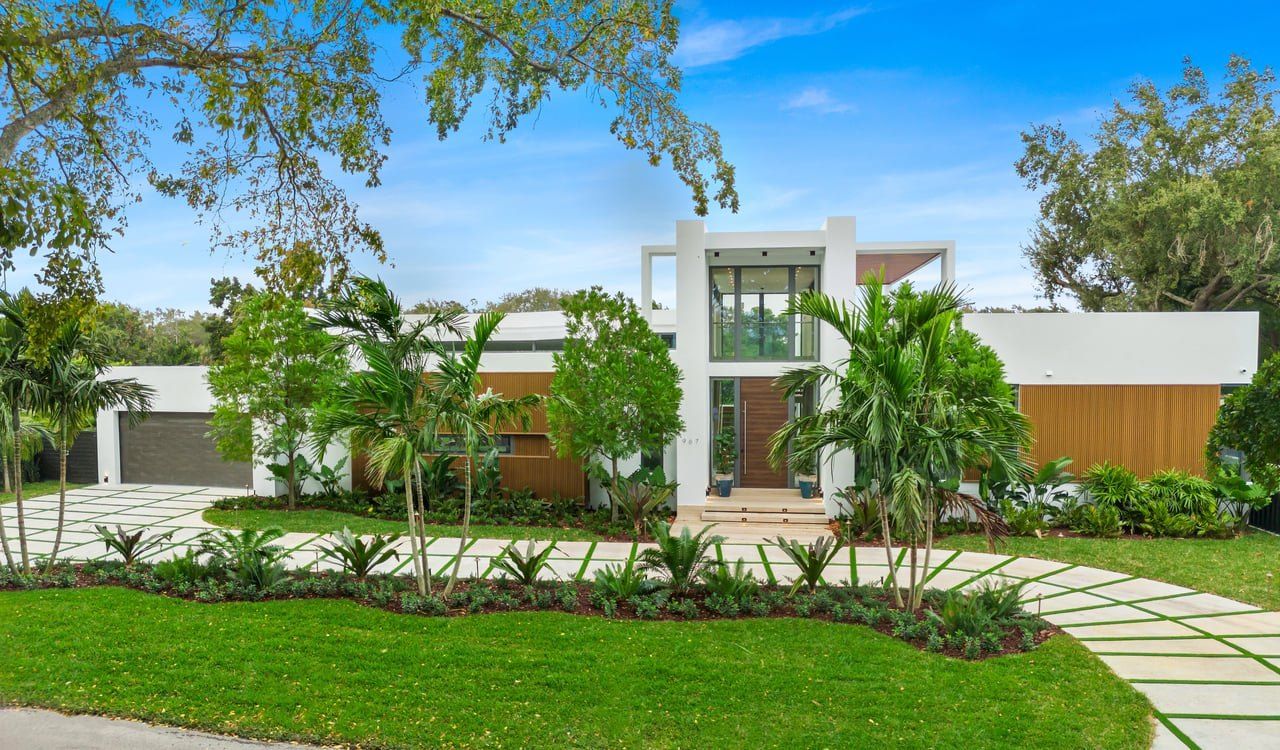 Street view of a modern white home with wood accents and a landscaped drive